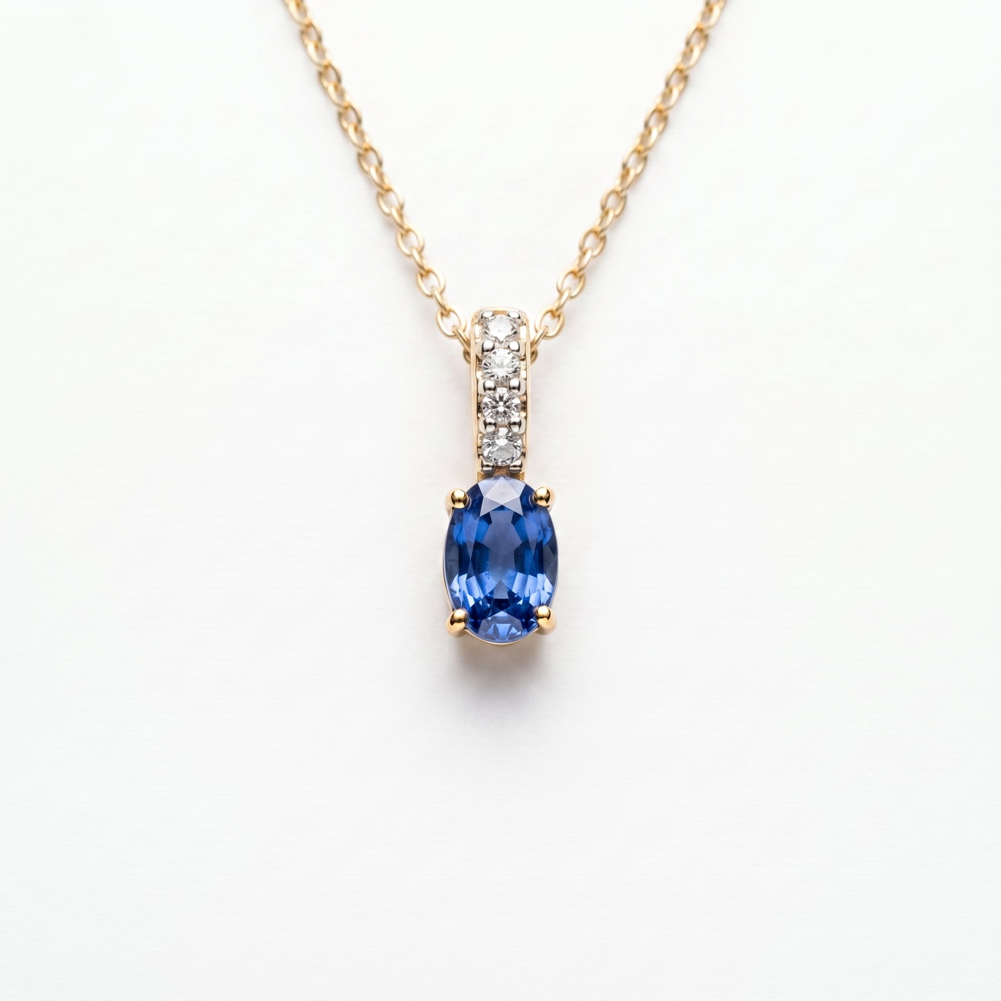A gold necklace with an oval blue sapphire pendant and a pavé-set diamond accent bar, on a wite background