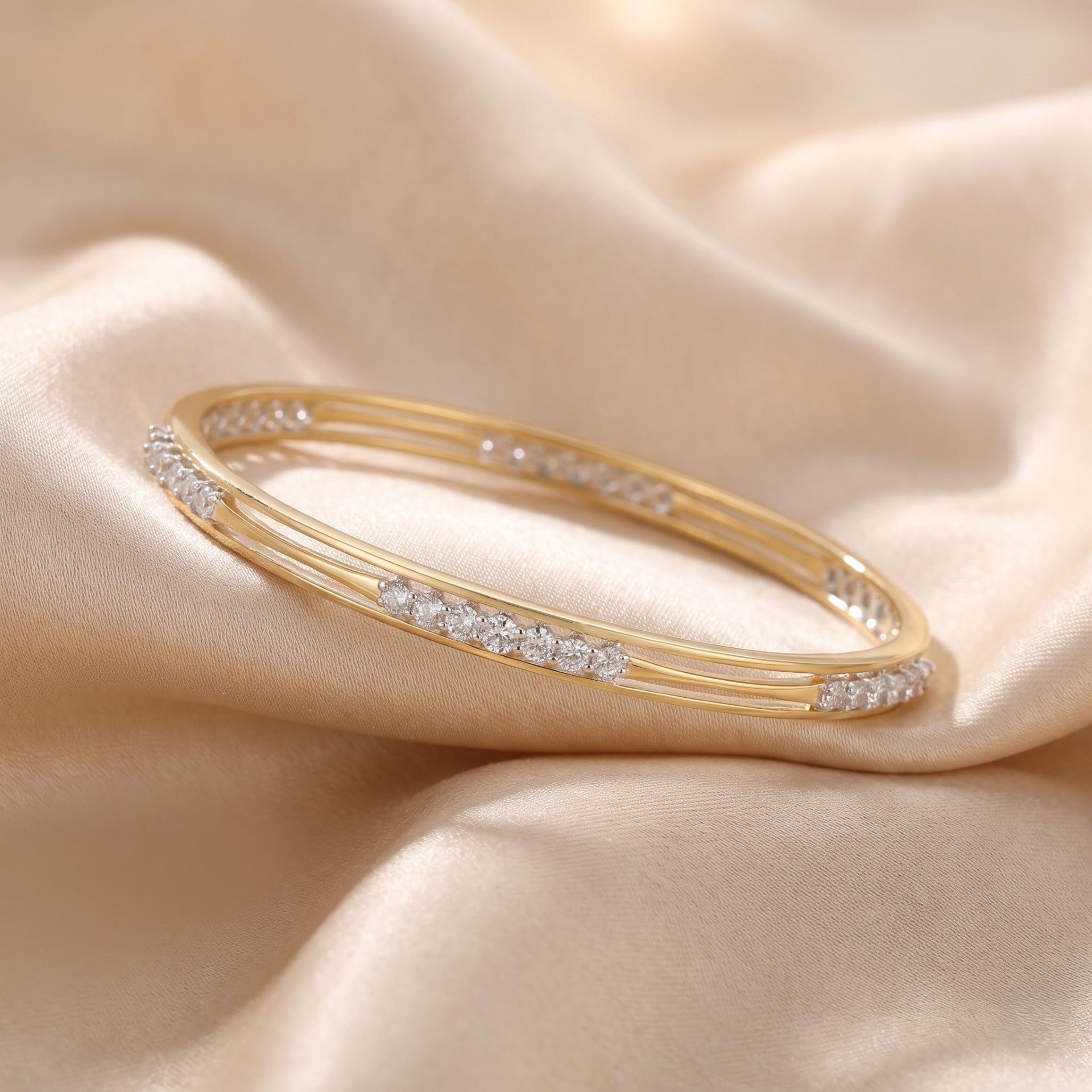 A gold bangle bracelet with rows of small clear stones, displayed on draped beige satin fabric.