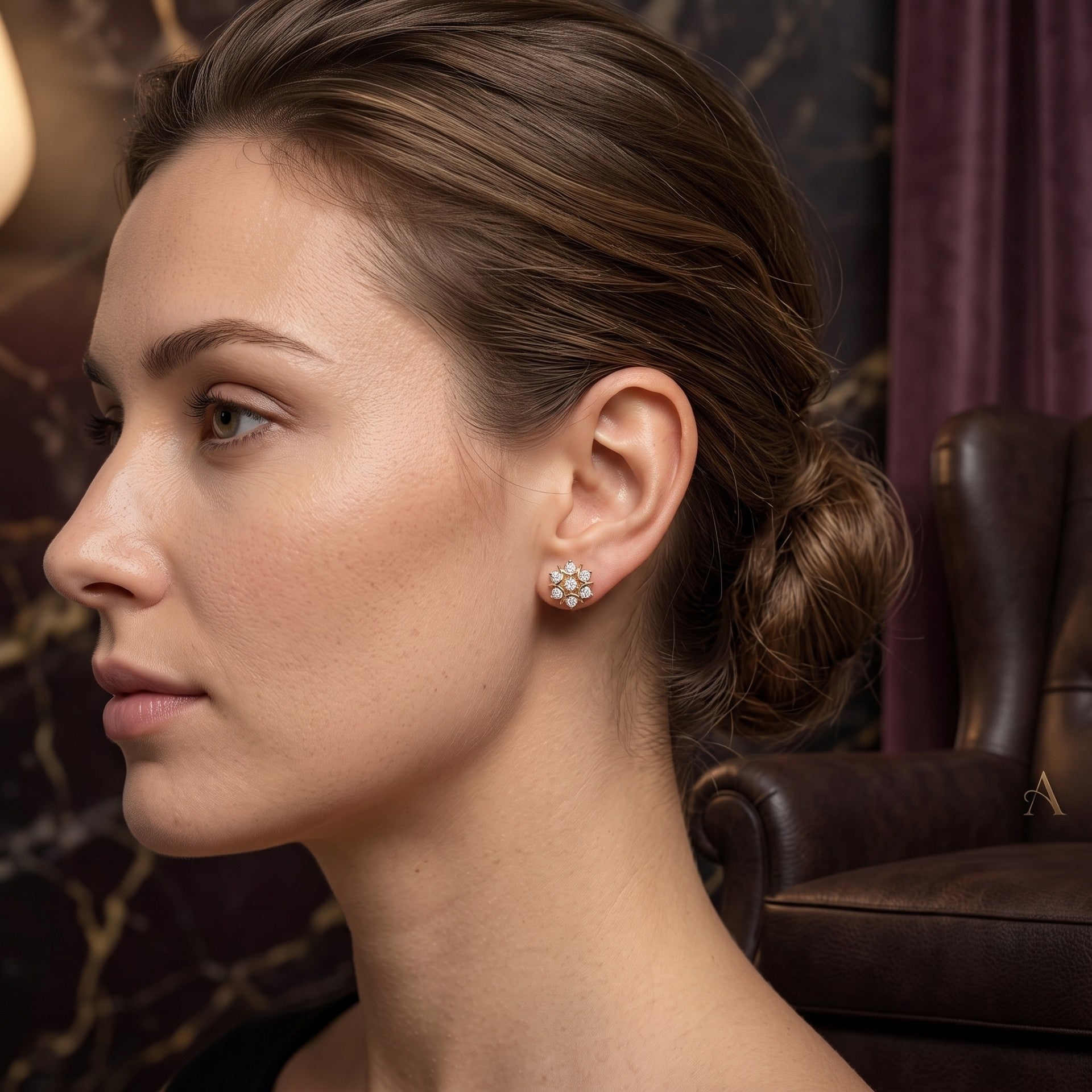 A woman in profile wearing a small floral stud earring with clear stones in a warm, elegant interior setting.