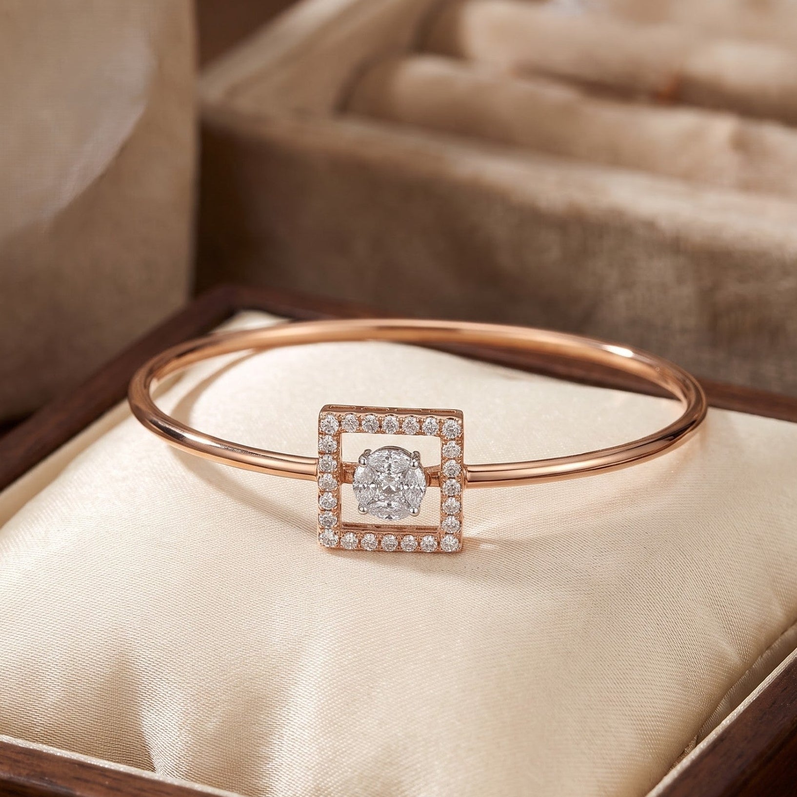 A rose gold bangle bracelet with a square diamond centerpiece, displayed on a cream satin cushion inside a wooden jewelry box.