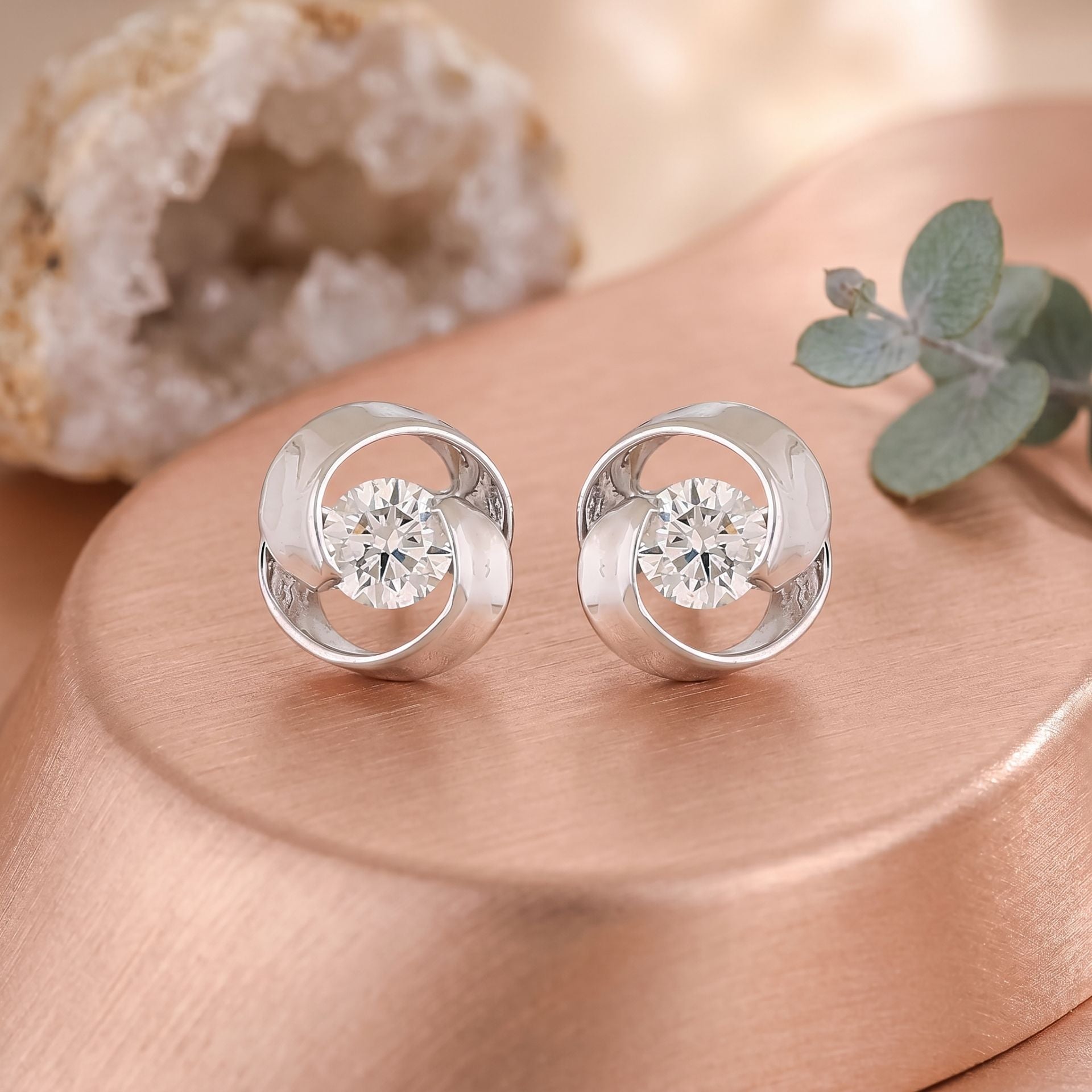 Silver earrings with circular design on a wooden surface with a natural rock and leaf in the background