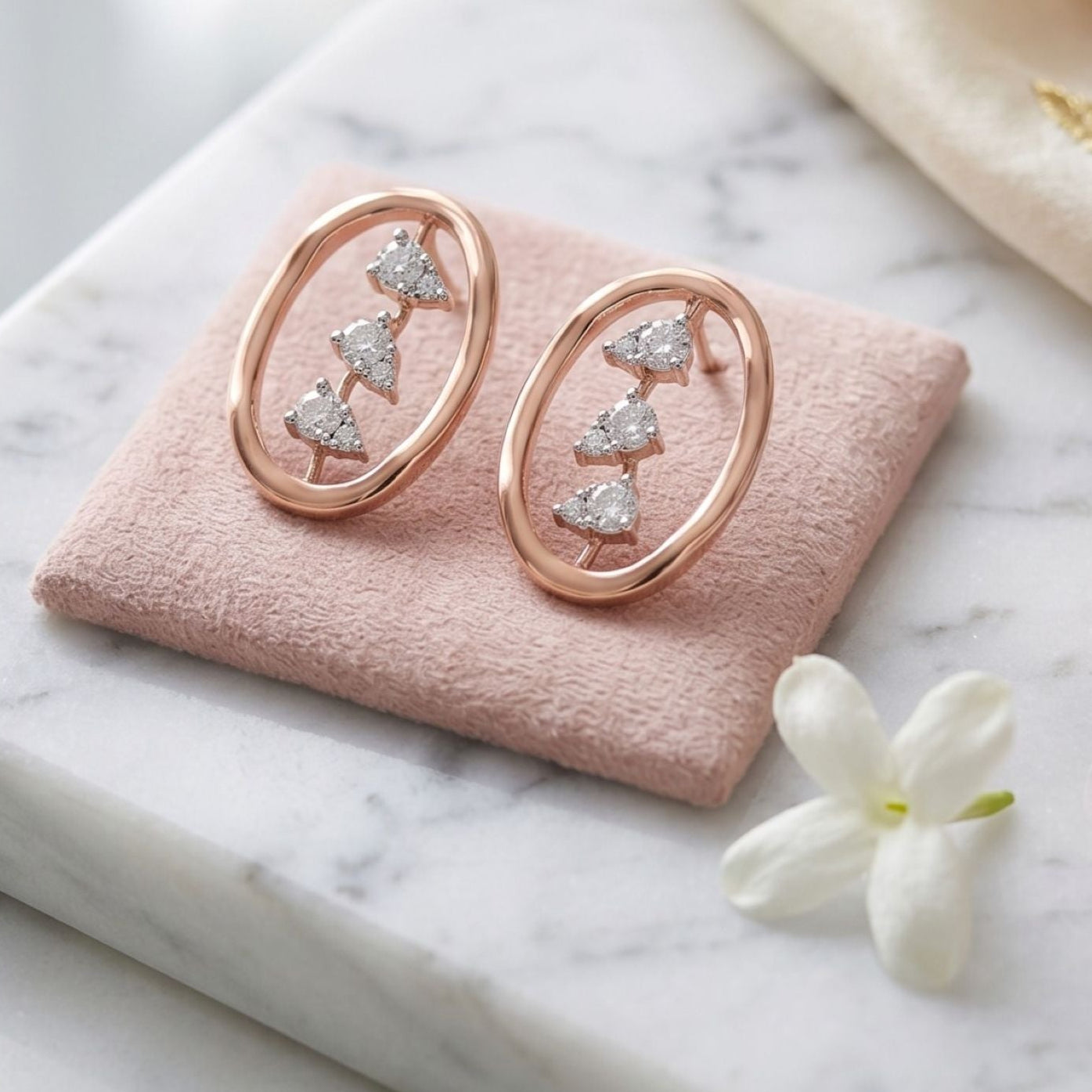 Rose gold earrings on a pink cushion with a marble surface and flowers.