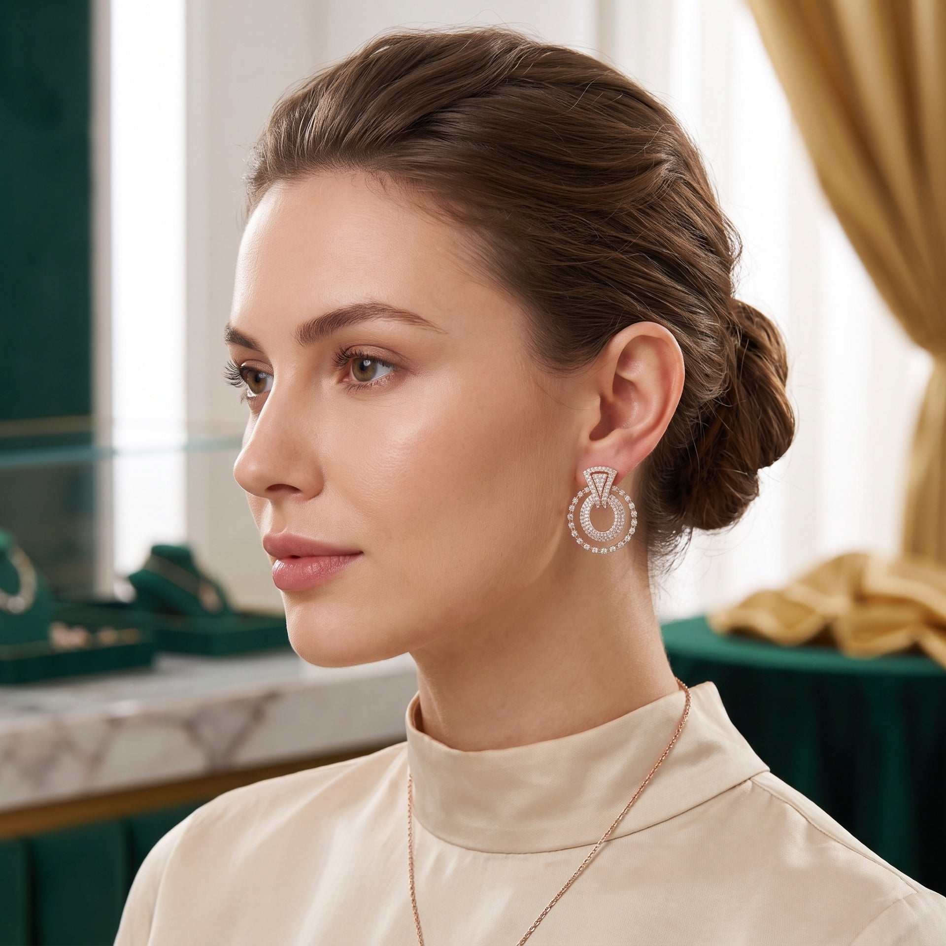A woman with her hair in a low bun is shown in profile wearing a delicate gold necklace and a matching drop nosepin. The earring features a central diamond-like stone surrounded by a halo of small clear stones.