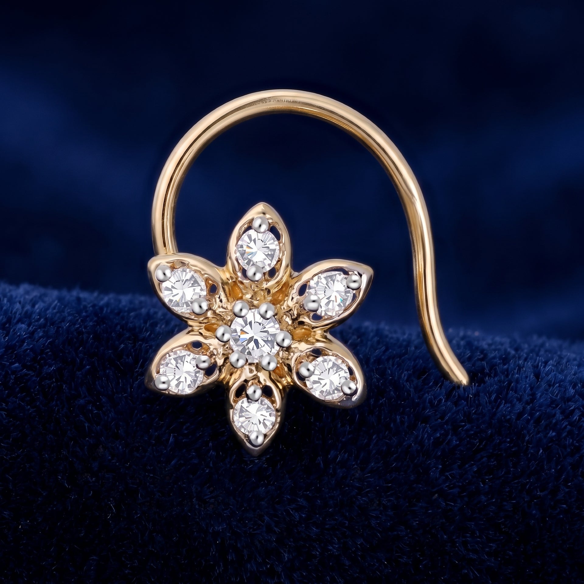 A gold flower-shaped earring with clear gemstones, displayed on a dark blue velvet surface.