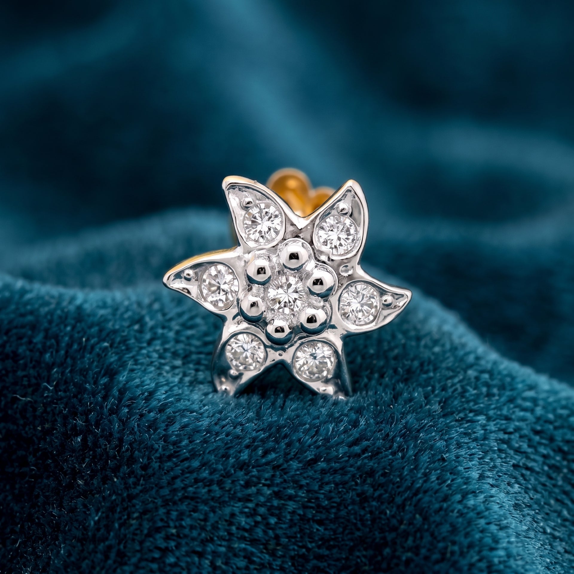 A silver-toned daffodil flower stud earring with clear cubic zirconia stones, resting on a textured dark teal velvet fabric background.