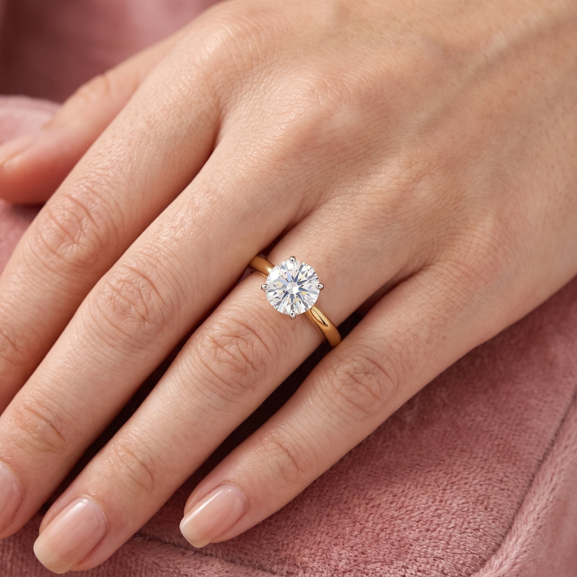 Gold ring with a diamond on a hand against a pink fabric background