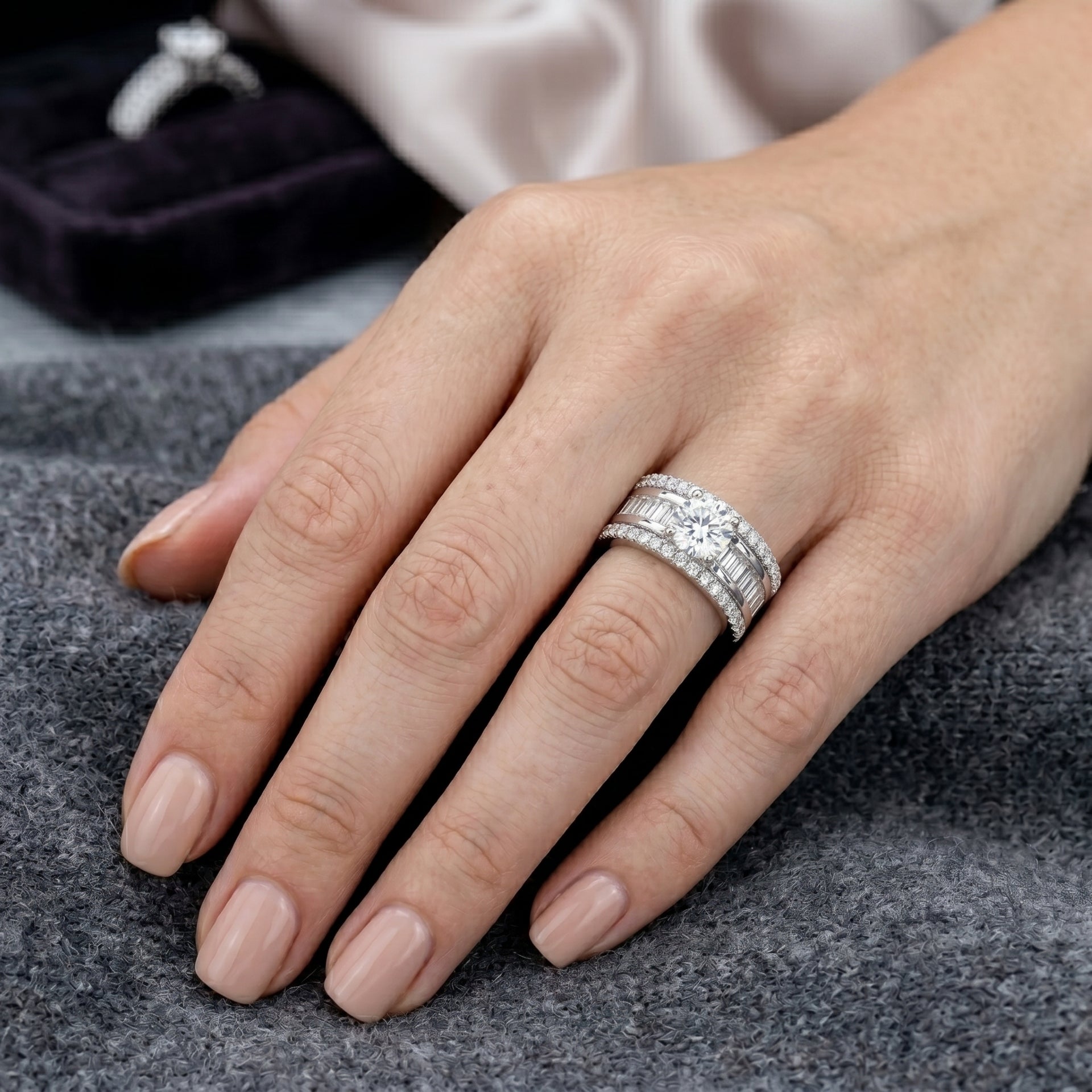 Hand wearing a diamond ring on a gray surface with a blurred background