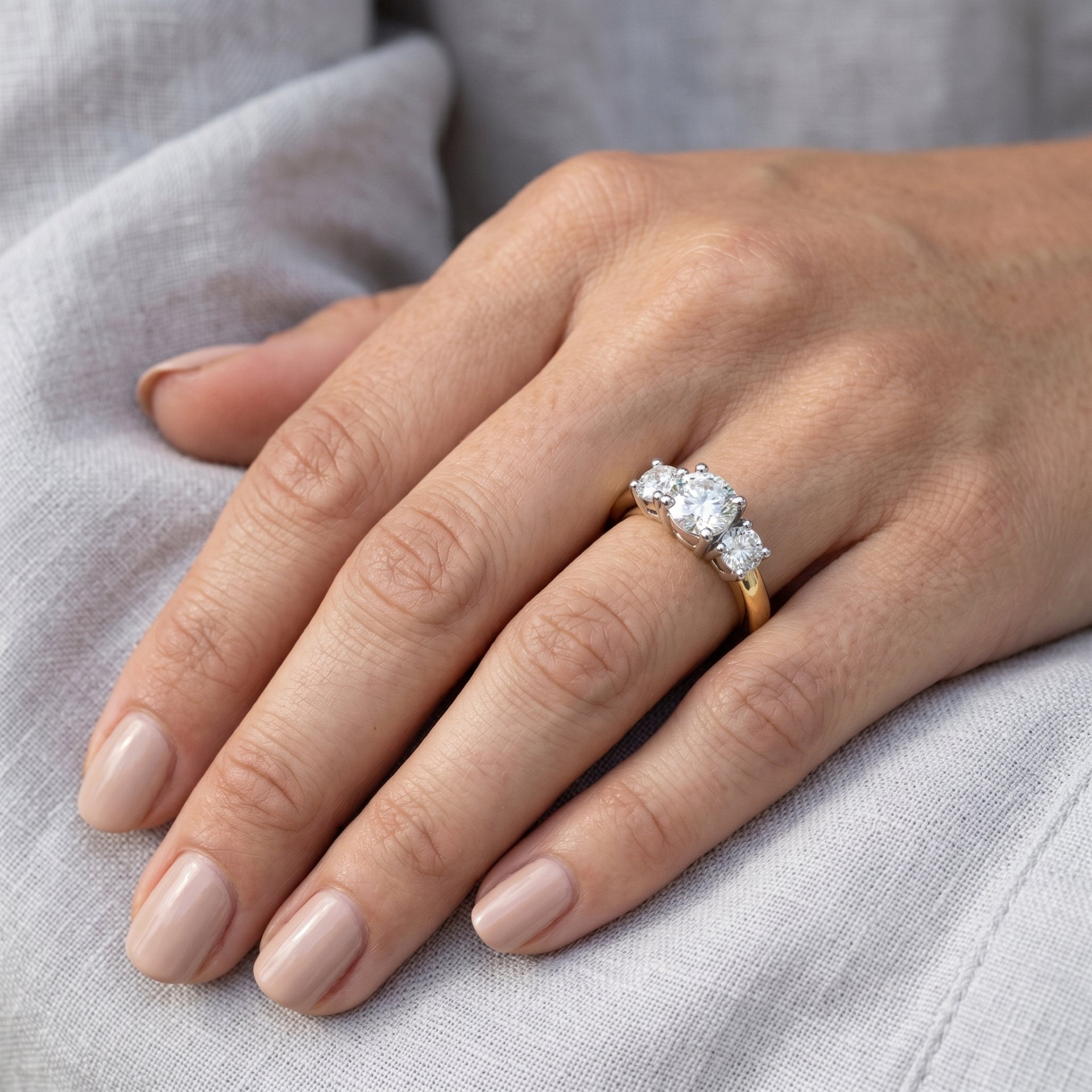 Hand wearing a diamond ring on a light gray fabric background