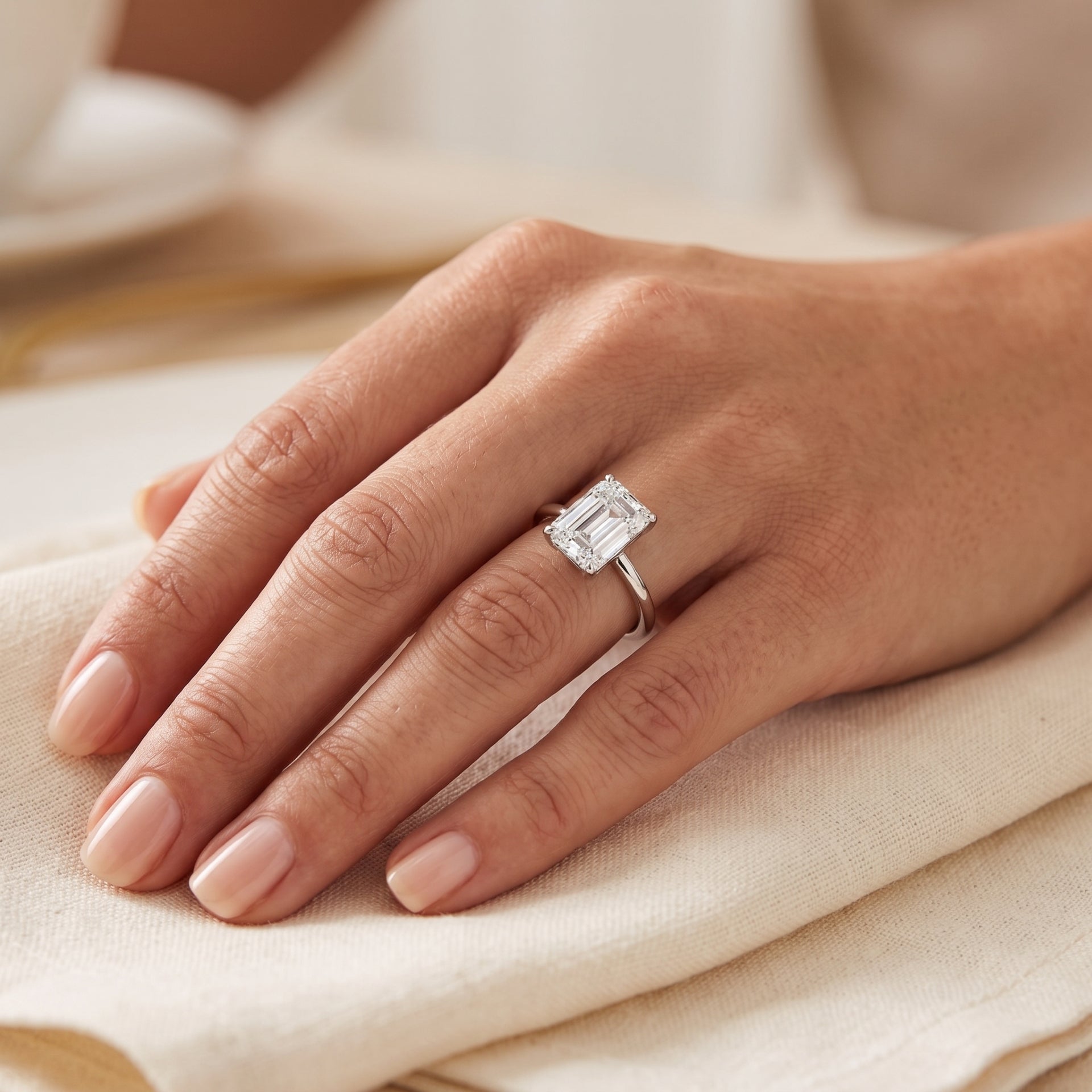 Hand wearing a diamond ring on a beige fabric background