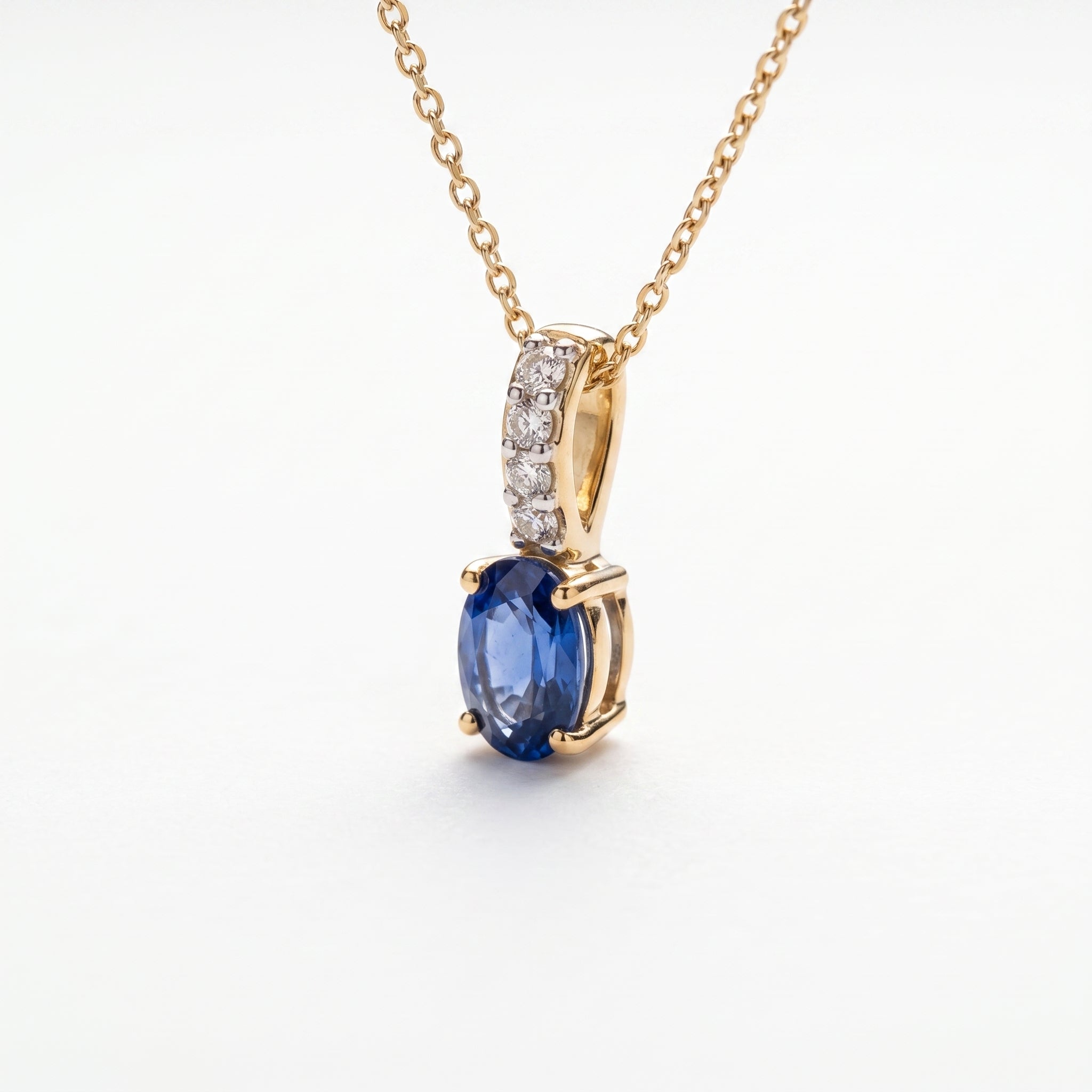 A gold necklace with an oval blue sapphire pendant and a pavé-set diamond accent bar, on a wite background