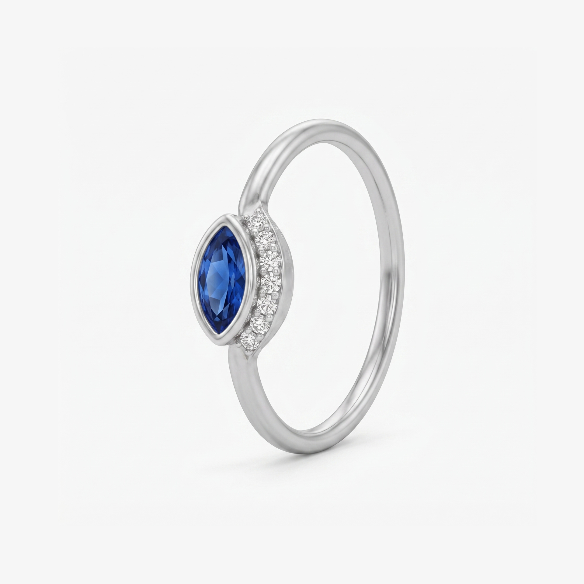 A silver ring featuring a marquise-cut blue sapphire center stone and a halo of small clear stones on the band, shown on a light gray background.