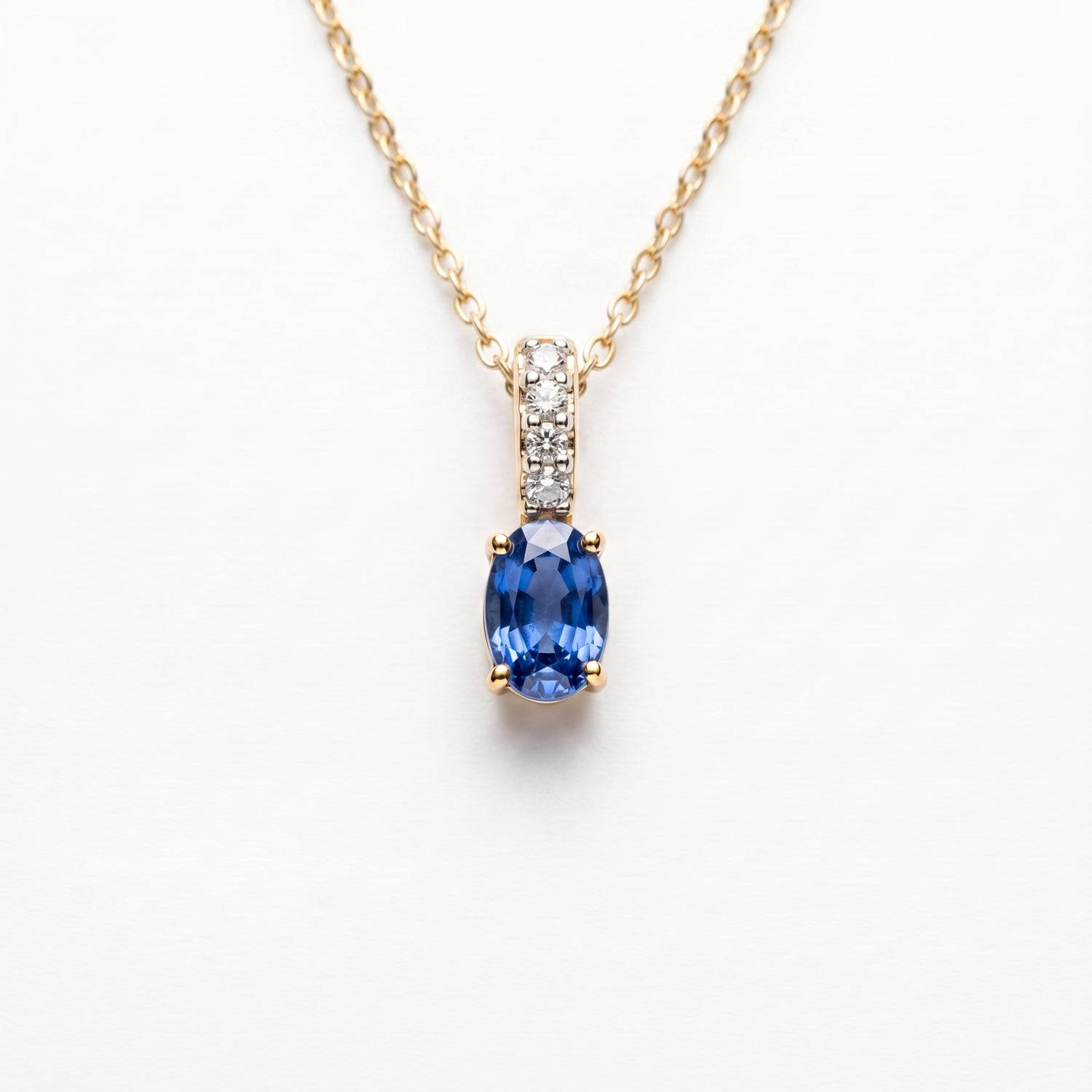A gold necklace with an oval blue sapphire pendant and a pavé-set diamond accent bar, on a wite background