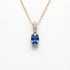 A gold necklace with an oval blue sapphire pendant and a pavé-set diamond accent bar, on a wite background