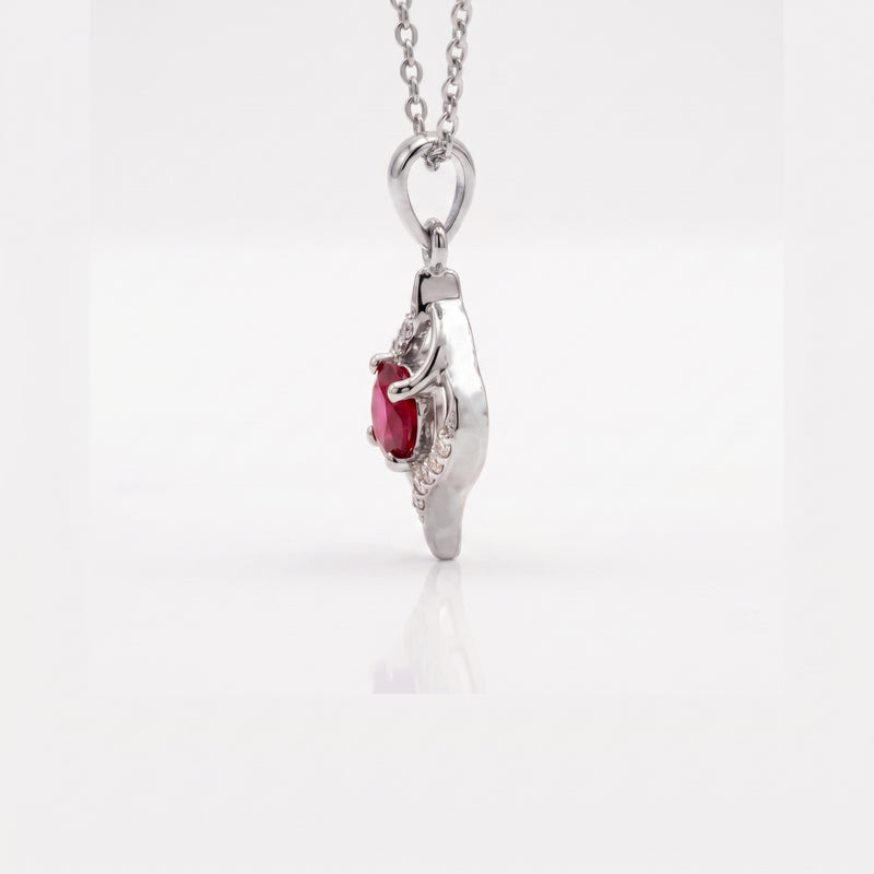 A silver pendant necklace featuring a small oval red gemstone surrounded by delicate clear stones, suspended from a silver chain against a light gray background.
