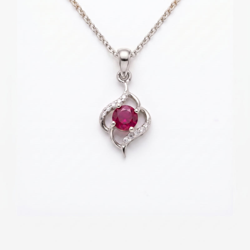 A silver pendant necklace featuring a central round pinkish-red gemstone surrounded by curved silver bands with small clear stones, suspended from a silver chain on a white background.