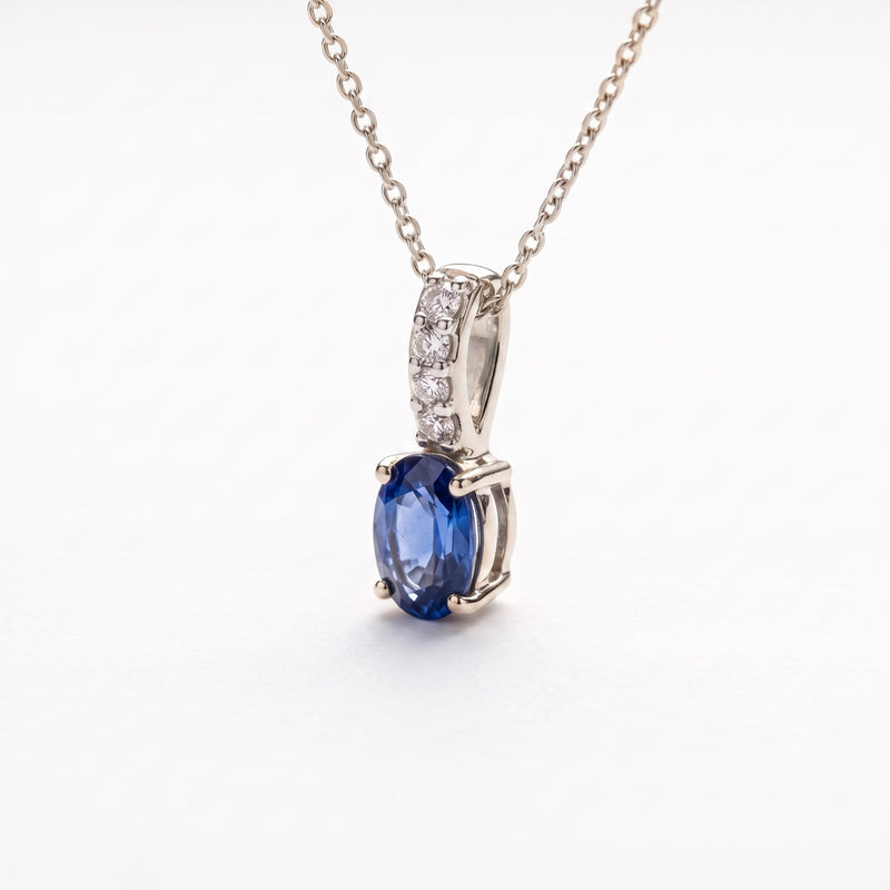 A silver pendant necklace featuring an oval-cut blue sapphire center stone and a top section set with small clear diamonds, shown on a white background.
