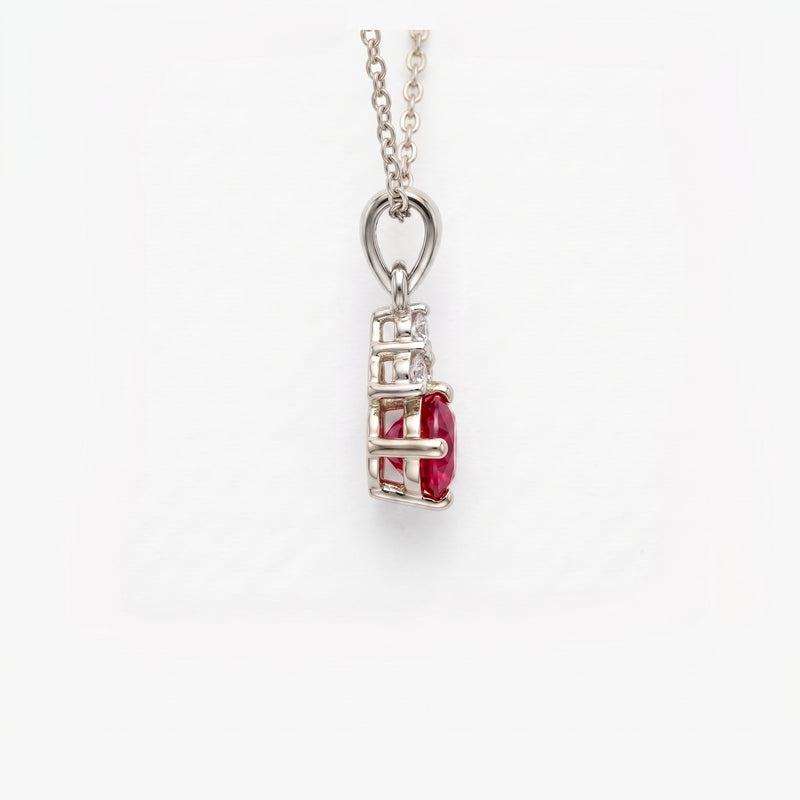 A silver pendant necklace featuring a rectangular cage setting with a central oval-cut red gemstone and small clear accent stones, suspended from a delicate silver chain against a plain white background.