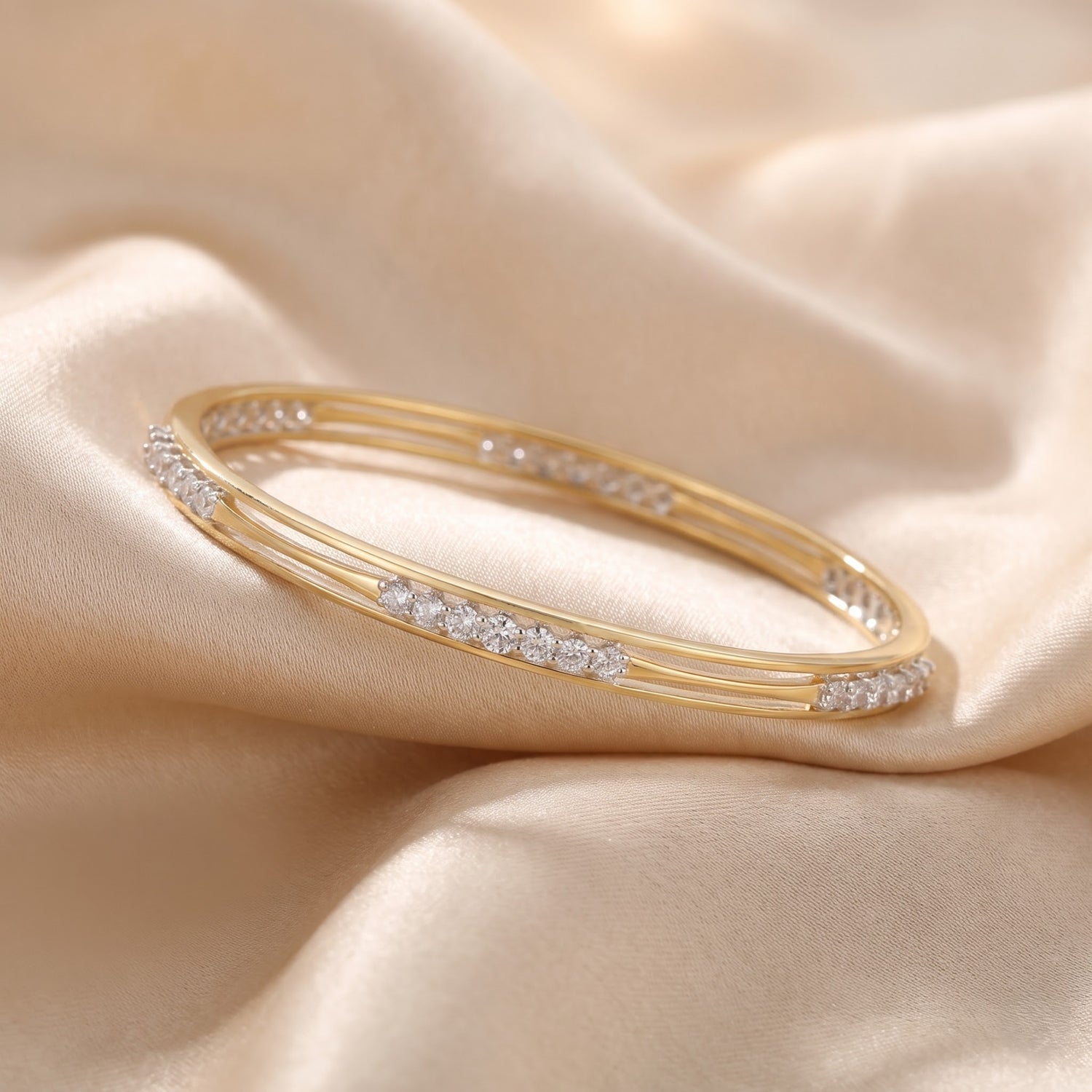 A gold bangle bracelet with rows of small clear stones, displayed on draped beige satin fabric.