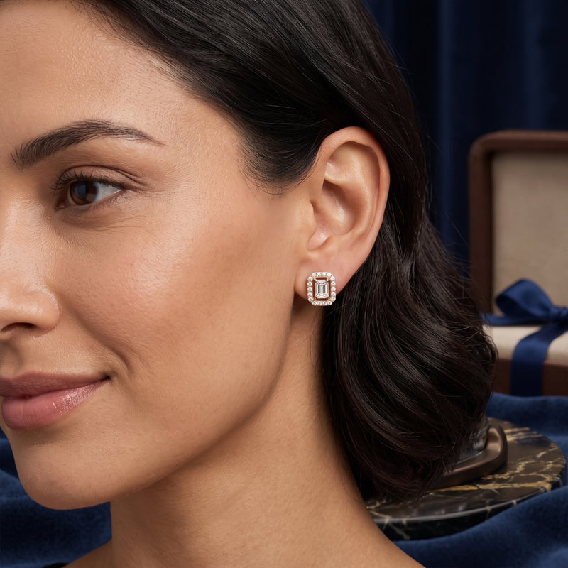 A close-up of a woman wearing a small rectangular stud earring with a silver-toned frame and clear stones, set against a dark blue velvet background.