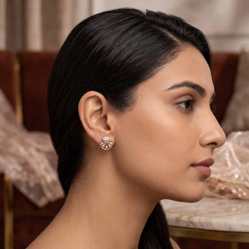 A close-up side profile of a woman with dark hair wearing a delicate gold-toned earring with a clear central stone and small surrounding accents, set against an elegant indoor background.
