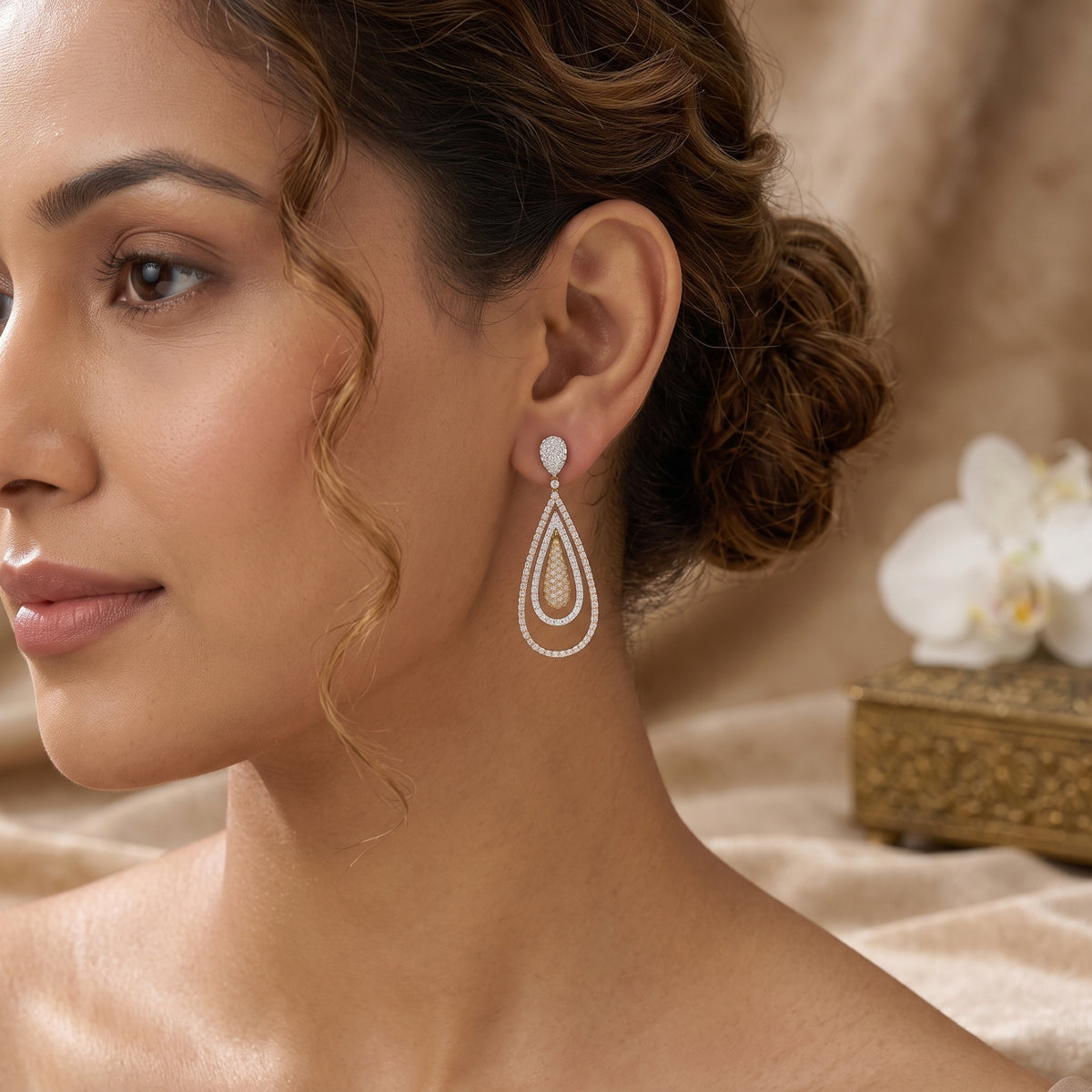 A woman wearing a teardrop-shaped drop earring with a white stone and silver-toned layered detailing, shown in a close-up portrait against a soft beige background with a white orchid flower.