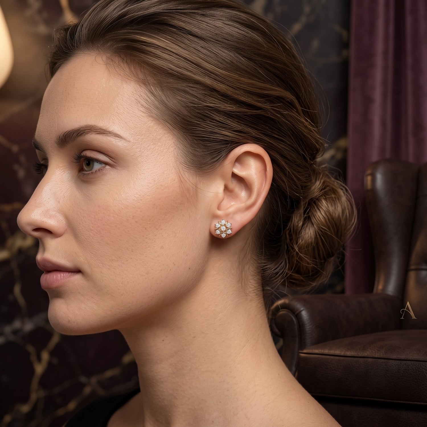 A woman in profile wearing a small floral stud earring with clear stones in a warm, elegant interior setting.