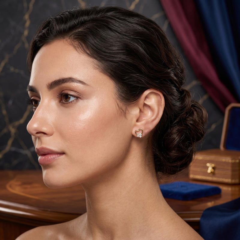 A woman in profile wearing a small diamond stud earring with a gold halo setting, photographed in an elegant interior setting with a dark marble wall and draped blue fabric in the background.