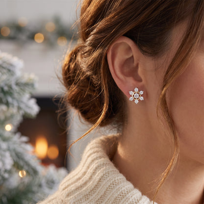 A close-up lifestyle shot of a woman wearing a silver snowflake-shaped stud earring with clear crystals, set against a warm, softly blurred holiday background with a fireplace and mistletoe.