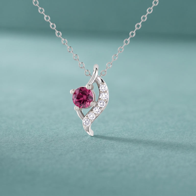 A silver necklace with a crescent-shaped pendant featuring a round pink gemstone and small clear stones, displayed on a soft teal background.