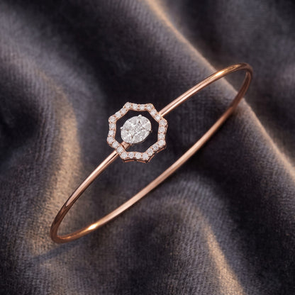 A rose gold bangle bracelet with a geometric octagonal center set with a halo of small clear stones and a central marquise-cut clear stone, displayed on a dark gray velvet fabric.