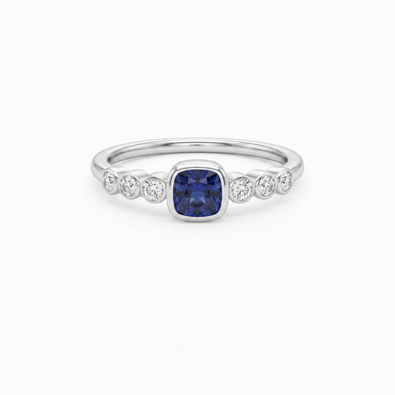 A silver band ring featuring a central cushion-cut blue sapphire gemstone, flanked by three small round-cut clear stones on each side, set against a plain white background.