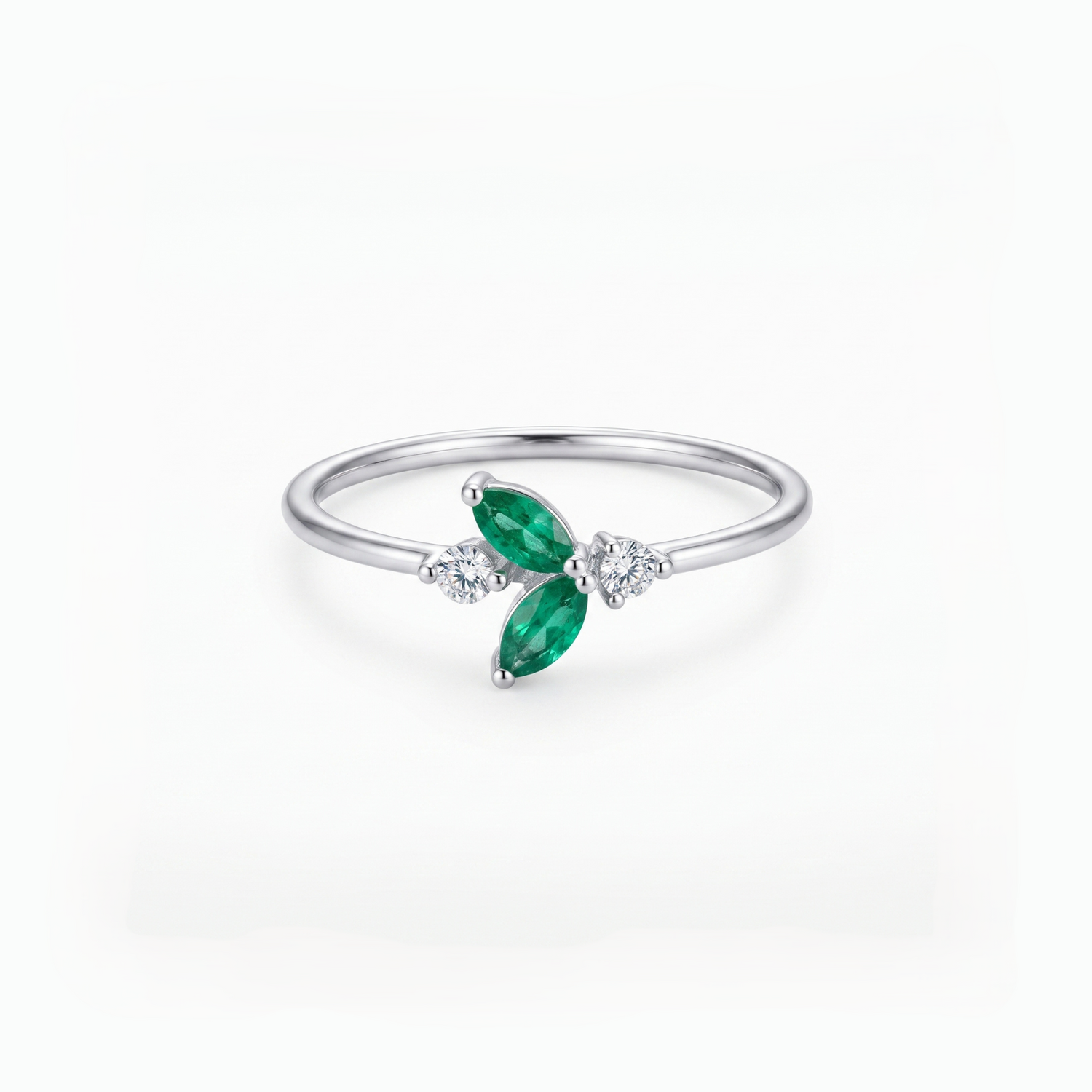 A silver ring featuring two marquise-cut green emeralds and small clear accent stones, set on a polished silver band against a clean white background.