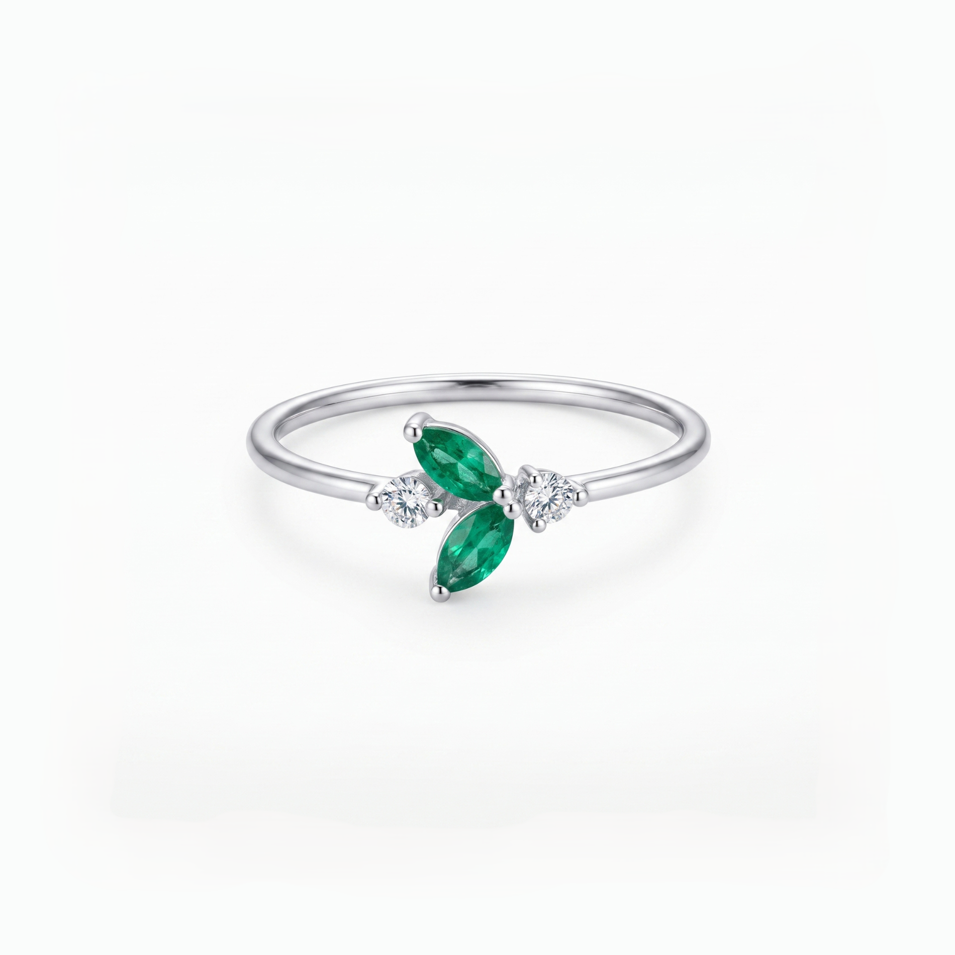 A silver ring featuring two marquise-cut green emeralds and small clear accent stones, set on a polished silver band against a clean white background.