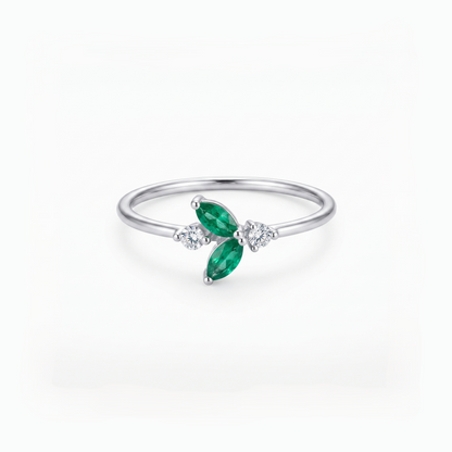 A silver ring featuring two marquise-cut green emeralds and small clear accent stones, set on a polished silver band against a clean white background.