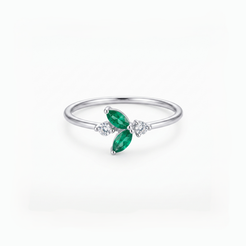 A silver ring featuring two marquise-cut green emeralds and small clear accent stones, set on a polished silver band against a clean white background.