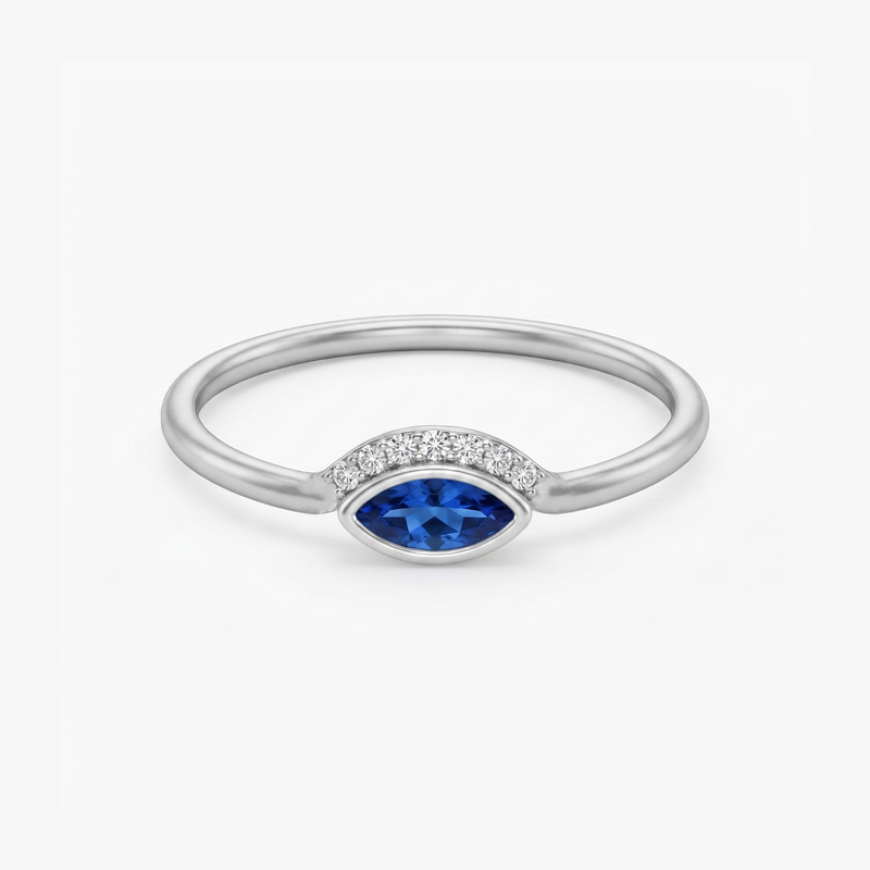 A silver ring featuring a marquise-cut blue gemstone in the center, flanked by a row of small clear stones on a clean white background.