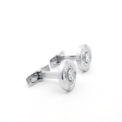 A pair of silver-toned round cufflinks with engraved outer rings and a clear central gemstone, displayed on a clean white background.