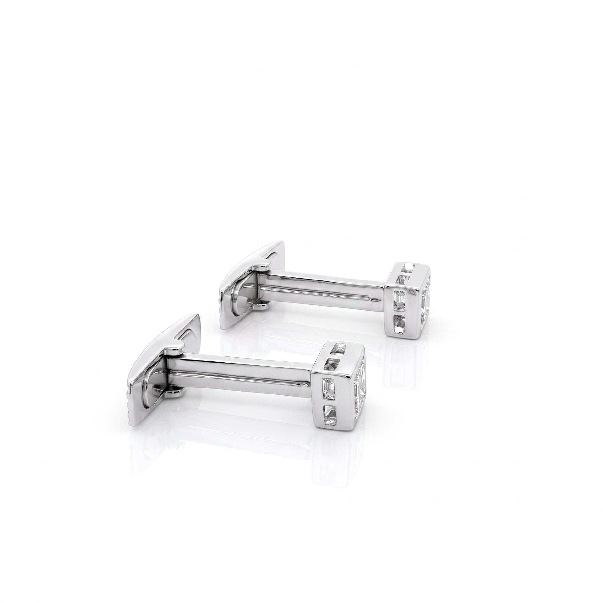A pair of silver-toned rectangular cufflinks with clear gemstone accents, displayed on a clean white reflective surface.