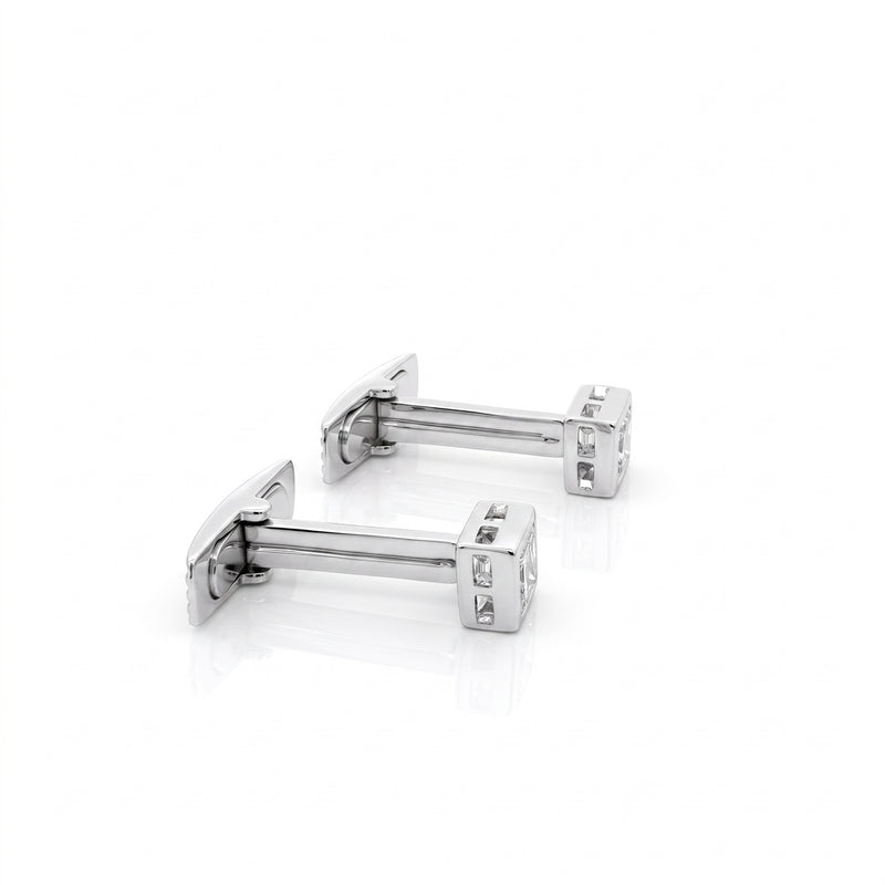 A pair of silver-toned rectangular cufflinks with clear gemstone accents, displayed on a clean white reflective surface.