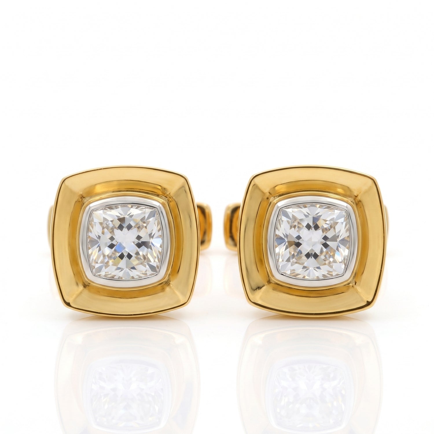 A pair of gold square stud earrings with cushion-cut clear gemstones, displayed on a reflective white surface.