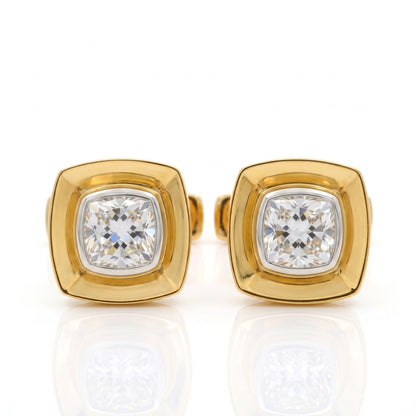A pair of gold square stud earrings with cushion-cut clear gemstones, displayed on a reflective white surface.