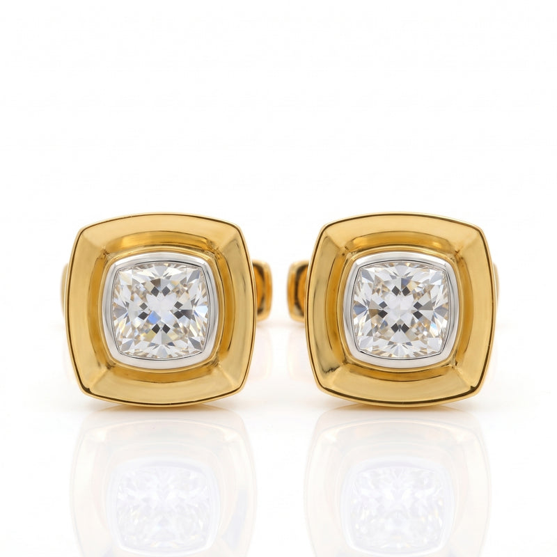 A pair of gold square stud earrings with cushion-cut clear gemstones, displayed on a reflective white surface.