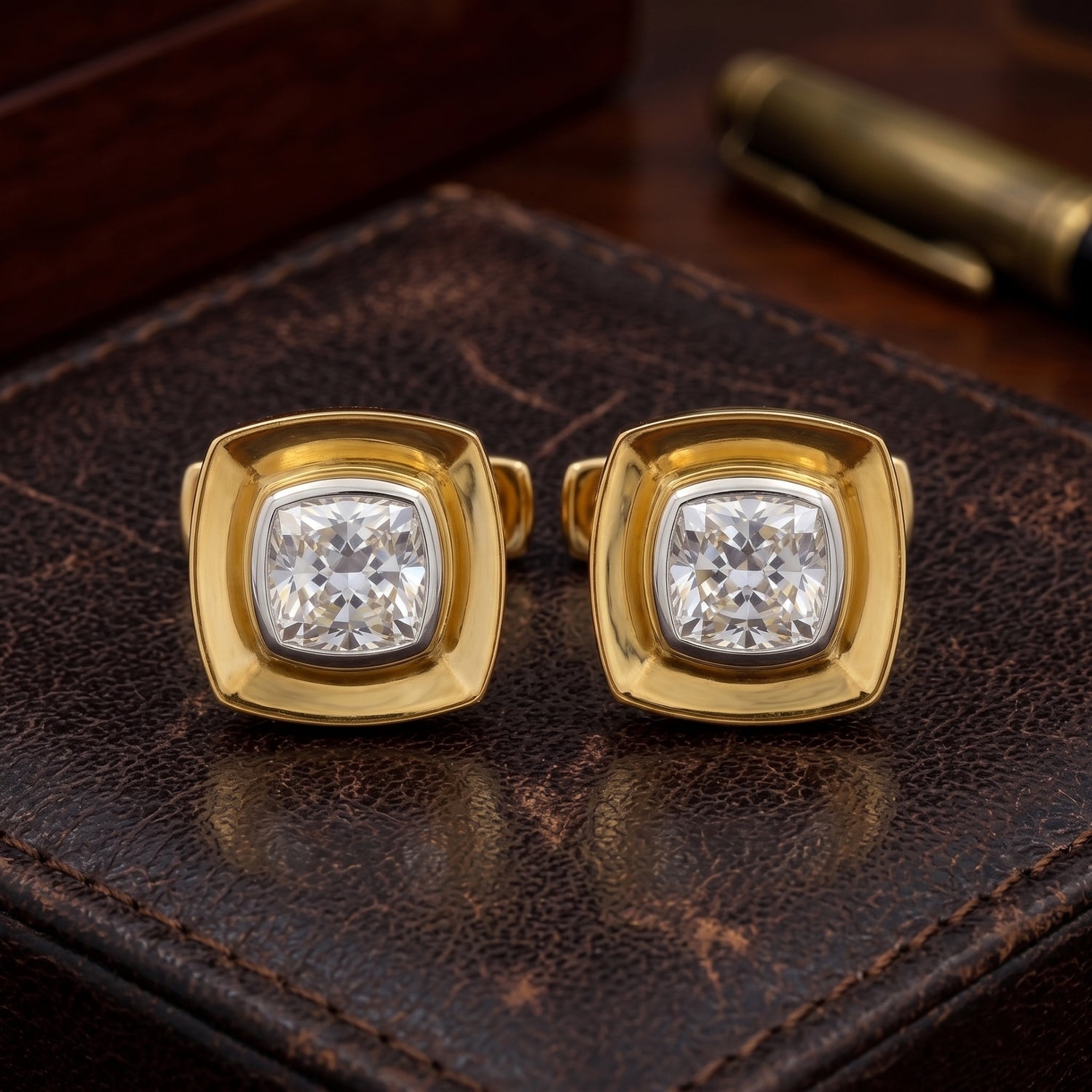 A pair of gold square stud earrings with cushion-cut clear gemstones, displayed on a textured dark brown leather surface.