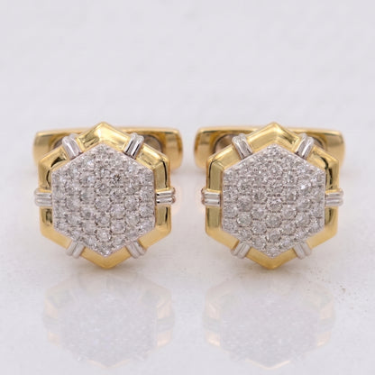 A pair of gold hexagonal stud earrings with pavé-set clear gemstones and small silver-toned side accents, shown on a light reflective surface.