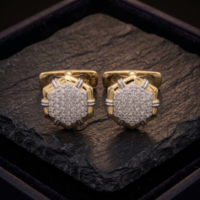 A pair of gold-toned cufflinks with pavé-set clear stones, displayed on a dark textured stone slab inside a black presentation box.