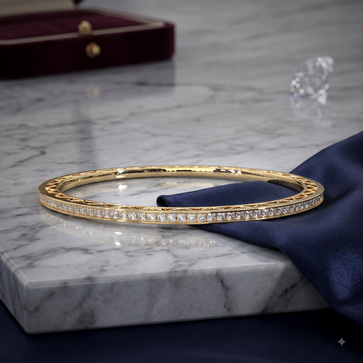 A gold bangle bracelet with a row of pavé-set clear stones, displayed on a dark blue satin cloth over a white marble slab.