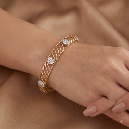 A gold bangle bracelet with three round-cut diamond accents, shown worn on a person&
