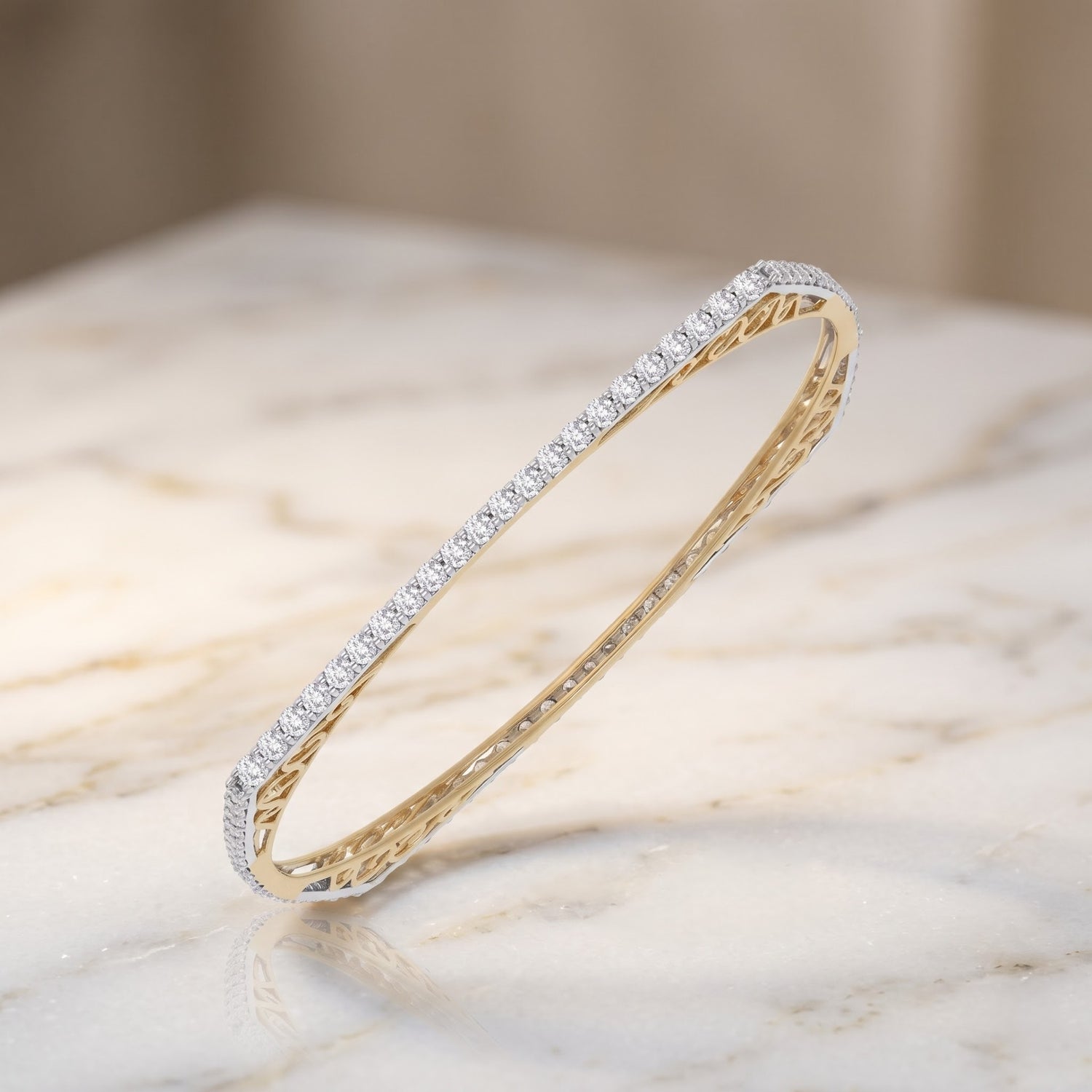 A slim oval bangle bracelet featuring a row of small clear stones on one side and a textured yellow gold finish on the inside, displayed on a light marble surface.