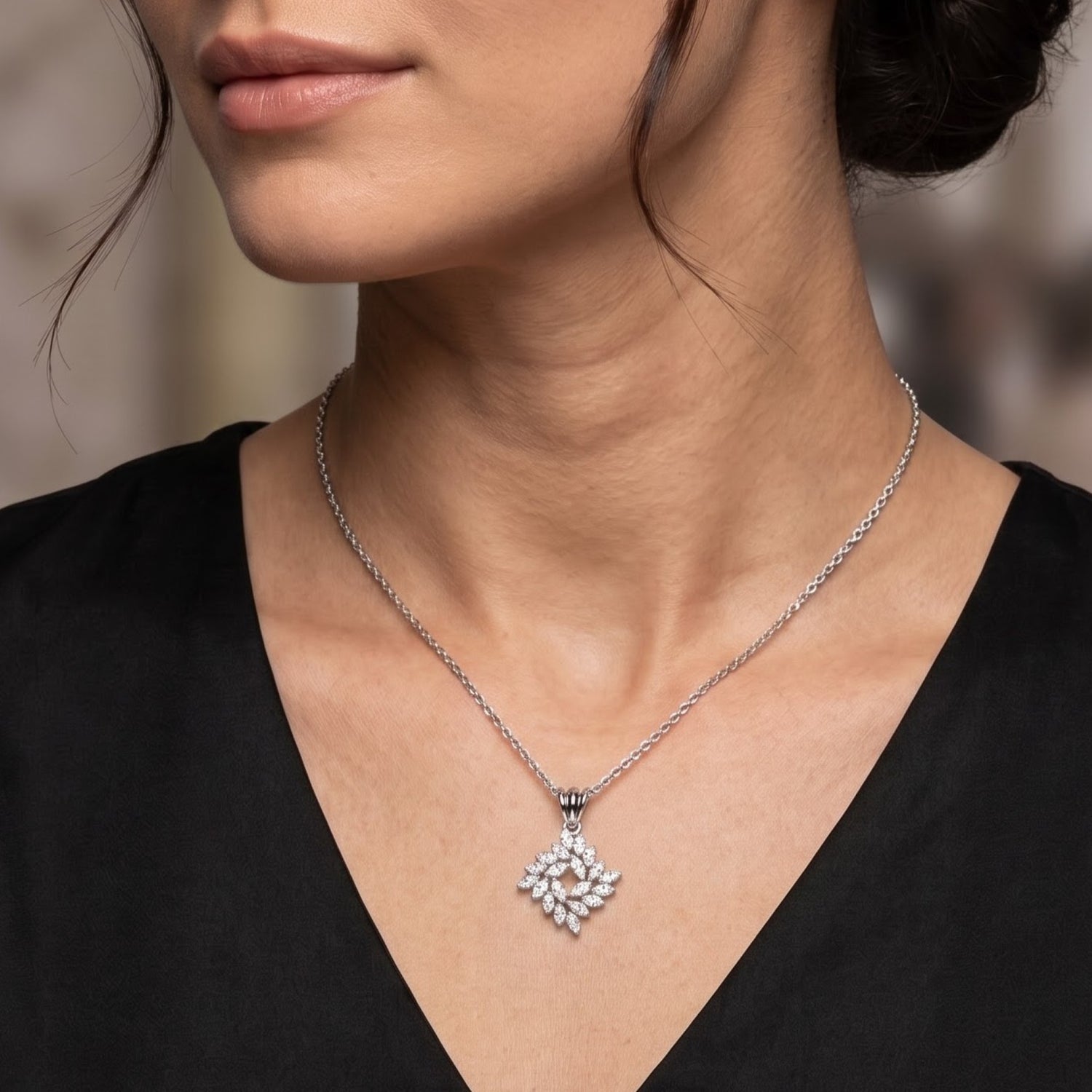 A close-up of a woman wearing a delicate silver chain necklace with a diamond-like floral pendant, styled with a black V-neck top.