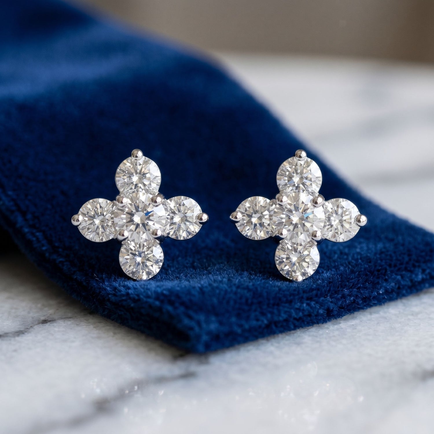 Flower-shaped diamond earrings on a blue velvet cushion with a marble background